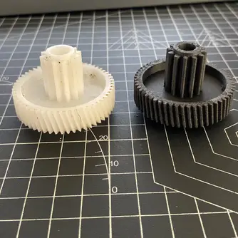 Roda gigi putih asli yang retak di samping roda gigi pengganti hitam hasil cetak 3D